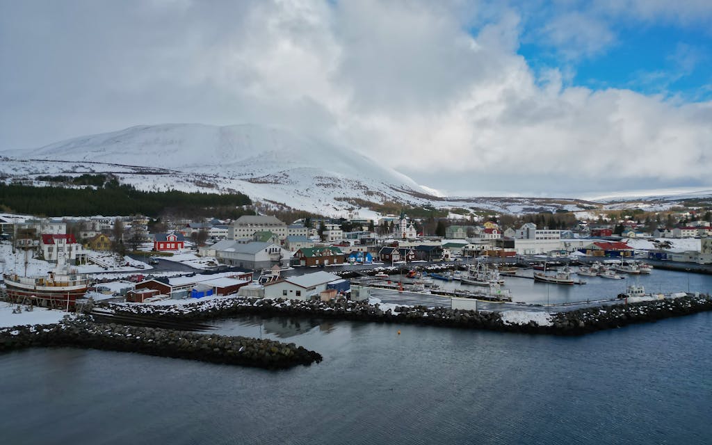 A picturesque harbor in Islandia, Iceland surrounded by snowy mountains and colorful buildings.